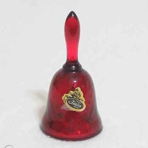 Puede incluir: Una campana de cristal rojo rubí con un mango largo. La campana tiene una base redondeada y una etiqueta dorada y blanca que dice "Fenton". Es probable que la campana sea un artículo decorativo.
