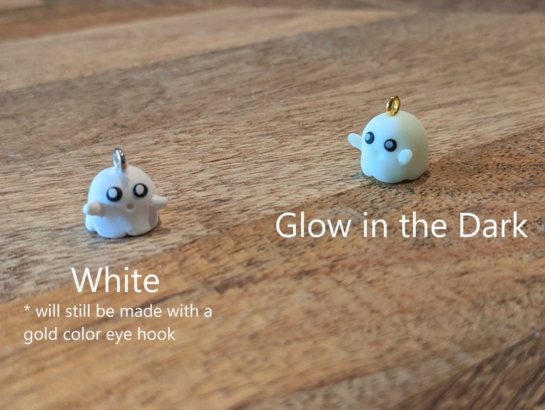Op de afbeelding: Twee kleine spookvormige ornamenten, een wit en een die in het donker gloeit. Beide hebben zwarte ogen en een gouden ooghaak.