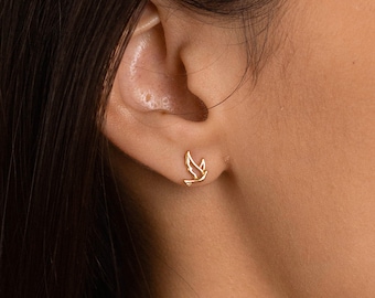 Pode incluir: Uma mulher usando um colar de corrente de ouro com um pequeno pingente de pássaro e um par de brincos de pássaro de ouro.