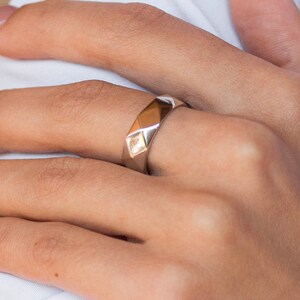 May include: A silver ring with a geometric design. The ring is on a person's finger.