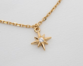 Puede incluir: Un collar de cadena dorada con un pequeño colgante de estrella con un cristal transparente en el centro.