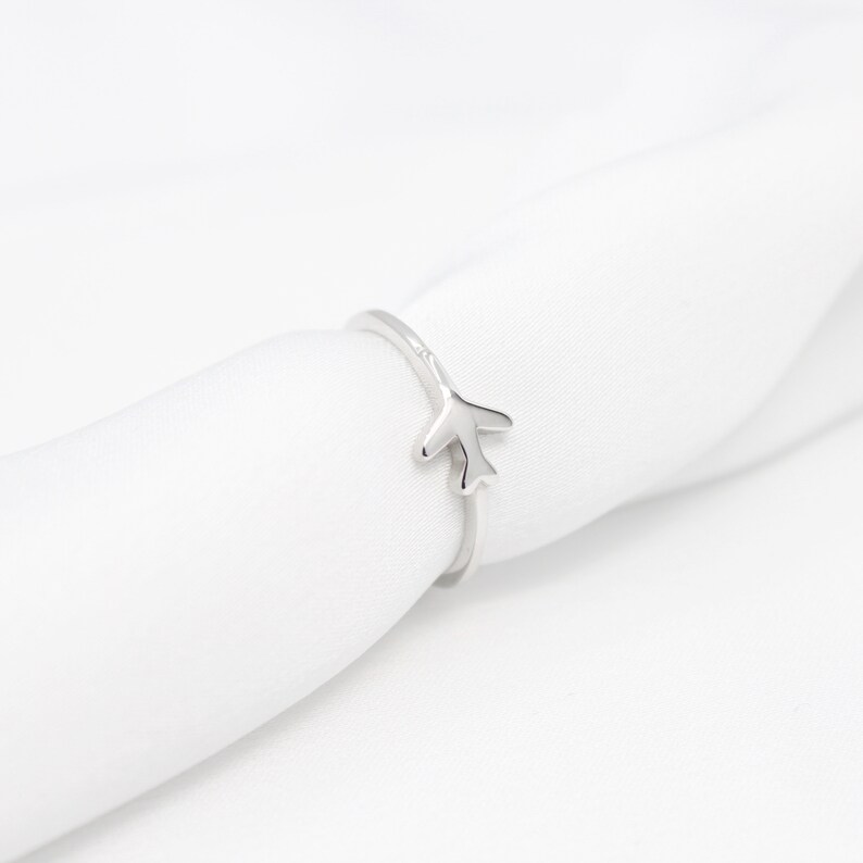 Op de afbeelding: Zilveren vliegtuigring op een witte stoffen achtergrond.