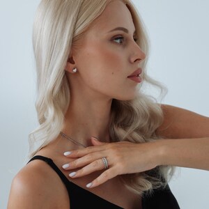 以下が含まれることがあります： 長いブロンドの髪をした女性が、黒いタンクトップと銀色のネックレスを着ています。彼女は指に銀色の指輪と銀色のイヤリングをしています。