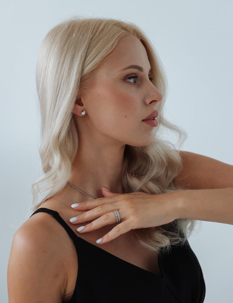 以下が含まれることがあります： 長いブロンドの髪をした女性が、黒いタンクトップと銀色のネックレスを着ています。彼女は指に銀色の指輪と銀色のイヤリングをしています。