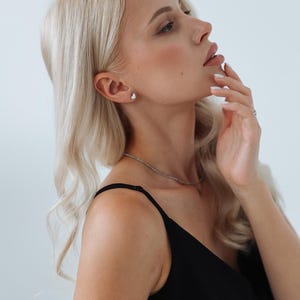 以下が含まれることがあります： 長いブロンドの髪をした女性が、黒いノースリーブのトップスを着ています。彼女は横を向いて、手で顔を触っています。