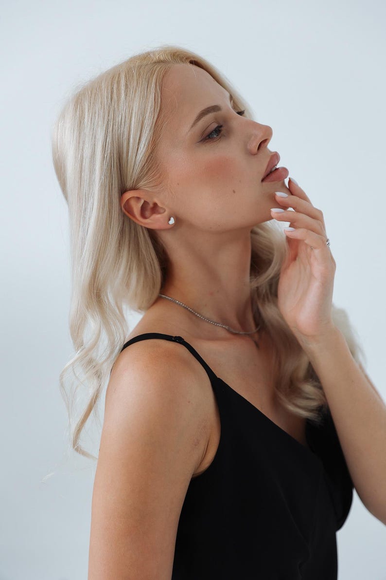 以下が含まれることがあります： 長いブロンドの髪をした女性が、黒いノースリーブのトップスを着ています。彼女は横を向いて、手で顔を触っています。