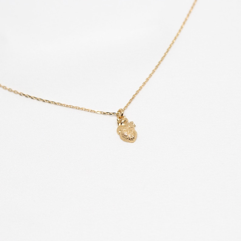 May include: A gold chain necklace with a small, textured heart pendant.