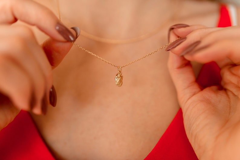 May include: A gold chain necklace with a small, textured, gold pendant in the shape of a heart.
