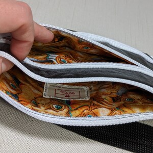 May include: Black leather zippered pouch with a white zipper and a white and orange fabric lining featuring a repeating pattern of cartoon faces. The pouch has a label that reads "Etsy Bob's Handmade Etsy Shop".
