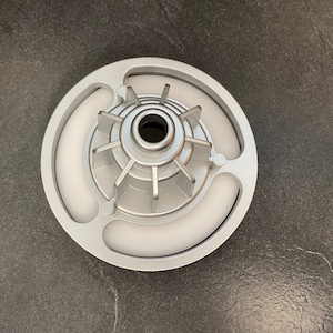 Könnte beinhalten: Ein silbernes Metallteil mit einer zentralen Nabe und mehreren Speichen. Die Nabe hat eine kreisförmige Öffnung in der Mitte. Das Teil ist von einem Ring mit drei erhabenen Abschnitten umgeben.