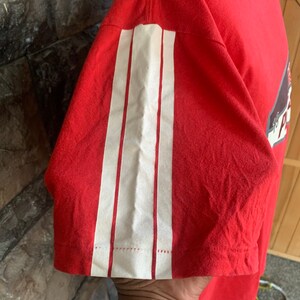 Op de afbeelding: Rood t-shirt met drie verticale witte strepen op de mouw. Het shirt is gemaakt van een zacht materiaal en heeft een klassieke ronde hals. De mouw is kort en de strepen zijn opgenaaid.