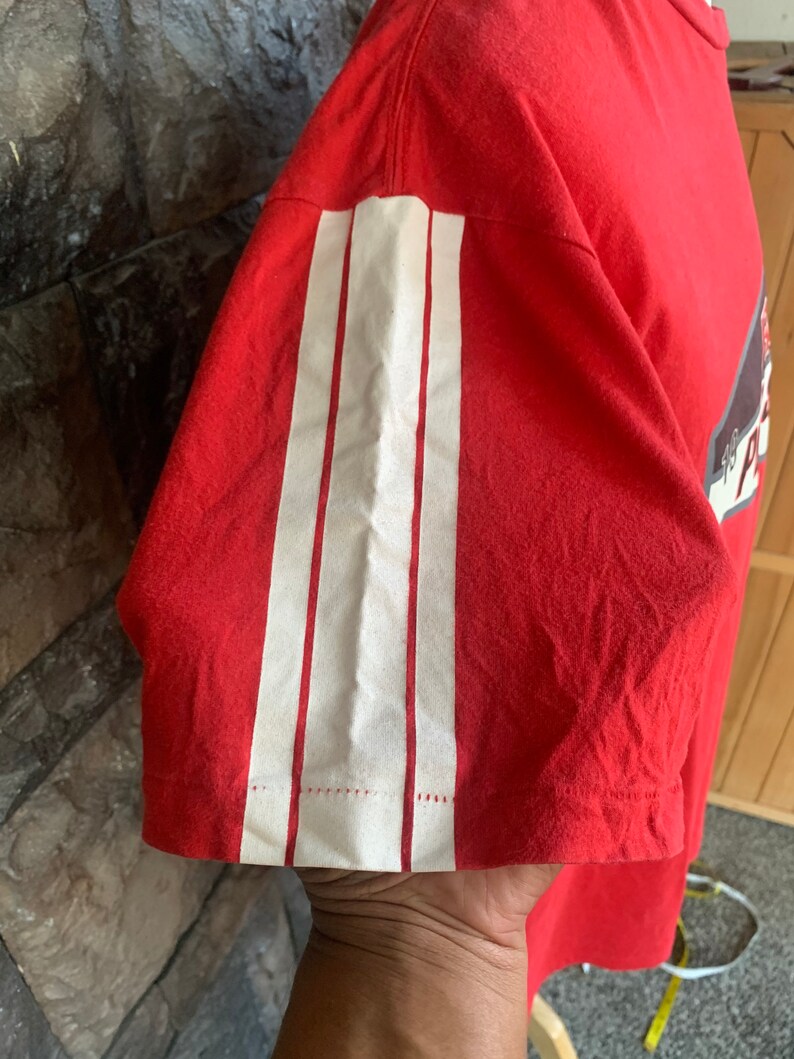 Op de afbeelding: Rood t-shirt met drie verticale witte strepen op de mouw. Het shirt is gemaakt van een zacht materiaal en heeft een klassieke ronde hals. De mouw is kort en de strepen zijn opgenaaid.