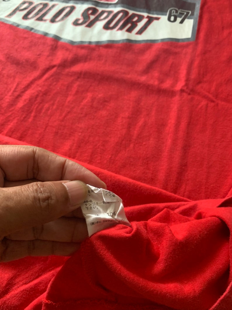 Op de afbeelding: Een rood Polo Sport T-shirt met een wit en grijs rechthoekig ontwerp over de borst. Het ontwerp bevat de woorden "POLO SPORT" en het nummer "67". Het shirt is gemaakt van een zacht, waarschijnlijk katoenen materiaal.