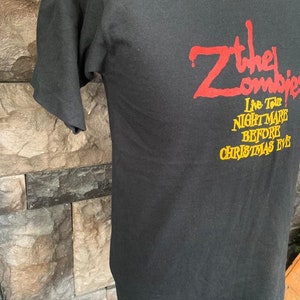 Peut inclure: T-shirt noir avec l'inscription "Z the Zombies" en rouge et "Live Tour! Nightmare Before Christmas Eve" en jaune. Le t-shirt est fait d'une mati&egrave;re douce et a des manches courtes.