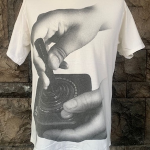 Puede incluir: Camiseta blanca con un estampado gráfico en blanco y negro de una mano sosteniendo un tocadiscos.