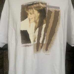 May include: White t-shirt featuring a brown and white image of singer Mary Chapin Carpenter. The image is a close-up of her face and has a faded, vintage look. The text "Mary Chapin Carpenter" is printed in a gold font across the top of the image.