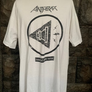 Puede incluir: Camiseta blanca con un gráfico en blanco y negro de un megáfono con rayos y el texto "Anthrax" y "[sound of white noise]" impreso en la parte delantera.
