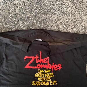 Peut inclure: T-shirt noir &agrave; manches longues avec l'inscription "Z the Zombies Live Tour Nightmare Before Christmas Eve" en rouge et jaune. Le t-shirt a un col rond et est fait d'une mati&egrave;re douce.
