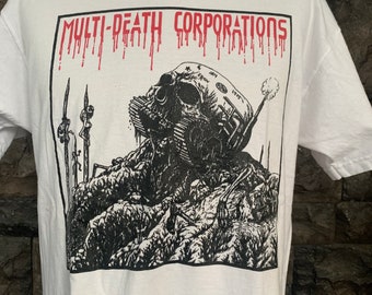 May include: White t-shirt with a black and white graphic print of a skull with a tank on top of it. The text "MULTI-DEATH CORPORATIONS" is printed in red above the graphic.