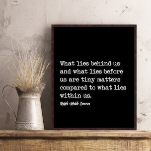 May include: A framed black print with white text quoting Ralph Waldo Emerson: "What lies behind us and what lies before us are tiny matters compared to what lies within us." A metal pitcher with dried grass sits to the left.