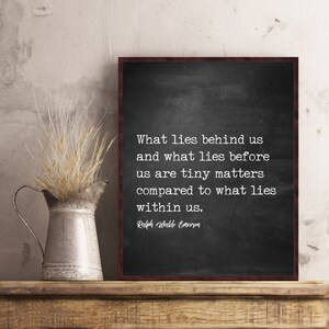 May include: A framed chalkboard print with a quote by Ralph Waldo Emerson. The quote reads, "What lies behind us and what lies before us are tiny matters compared to what lies within us." A metal pitcher with dried wheat is on a wooden shelf.