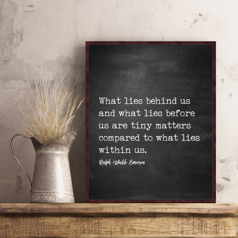 May include: A framed chalkboard print with a quote by Ralph Waldo Emerson. The quote reads, "What lies behind us and what lies before us are tiny matters compared to what lies within us." A metal pitcher with dried wheat is on a wooden shelf.