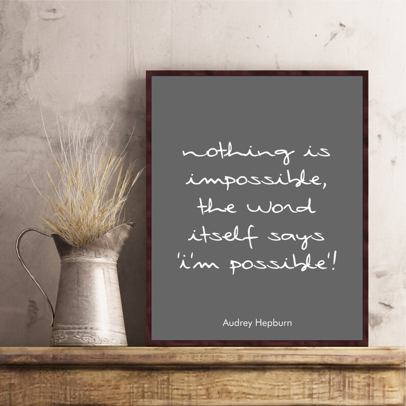 May include: A gray framed print with a white inspirational quote by Audrey Hepburn: "nothing is impossible, the word itself says 'i'm possible!"