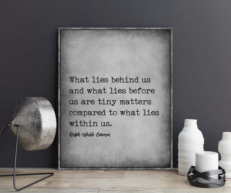 May include: A framed print with a gray background features a quote by Ralph Waldo Emerson: "What lies behind us and what lies before us are tiny matters compared to what lies within us." Decorative items are on a wooden surface.