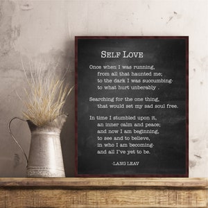 May include: Black and white typography print on a chalkboard background with a wooden frame. The print features a poem about self-love by Lang Leav. The poem reads: "Once when I was running, from all that haunted me; to the dark I was succumbing- to what hurt unbearably. Searching for the one thing, that would set my sad soul free. In time I stumbled upon it, an inner calm and peace; and now I am beginning, to see and to believe, in who I am becoming- and all I've yet to be. -Lang Leav"