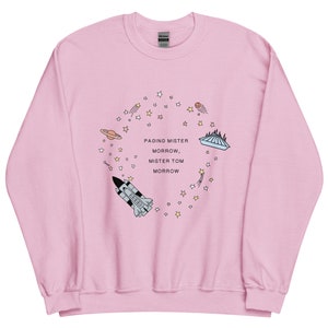 Könnte beinhalten: Hellrosa Sweatshirt mit einem kreisförmigen Design, das eine Rakete, Planeten, Sterne und den Text "Paging Mister Morrow, Mister Tom Morrow" zeigt. Das Design ist im Cartoon-Stil mit Pastellfarben gehalten.