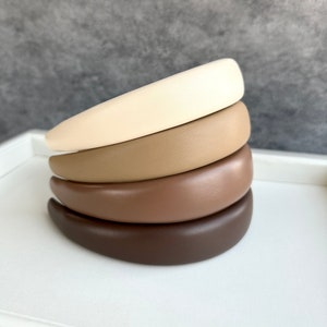 Könnte beinhalten: Vier stapelbare Haarbänder in Brauntönen, Beige und Creme. Die Haarbänder sind aus glattem Kunstleder gefertigt.