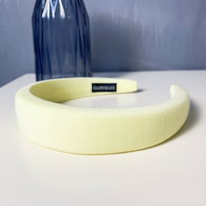 May include: A pale yellow headband with a black "Handmade" label. The headband is made of a soft, padded material.