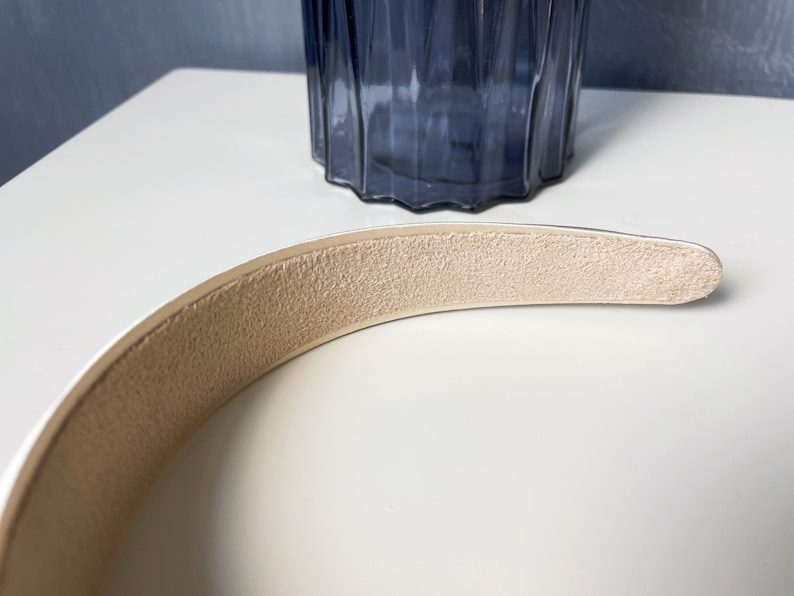 K&ouml;nnte beinhalten: Ein wei&szlig;es Stirnband mit einem beigefarbenen, Wildleder-&auml;hnlichen Futter. Das Stirnband ist gebogen und hat eine glatte, polierte Oberfl&auml;che.