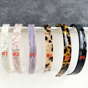 May include: Six different plastic headbands in various patterns. The headbands are numbered 1 through 6.  #1 is white with a pearlescent finish. #2 is pink with a pearlescent finish. #3 is light purple with a marbled finish. #4 is brown and white with a tortoise shell pattern. #5 is brown and black with a tortoise shell pattern. #6 is black with a marbled finish.