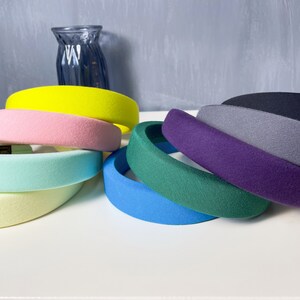 May include: A set of eight wide headbands in various colors, including yellow, pink, light blue, light green, blue, green, purple, and gray. The headbands are made of a soft, plush material.