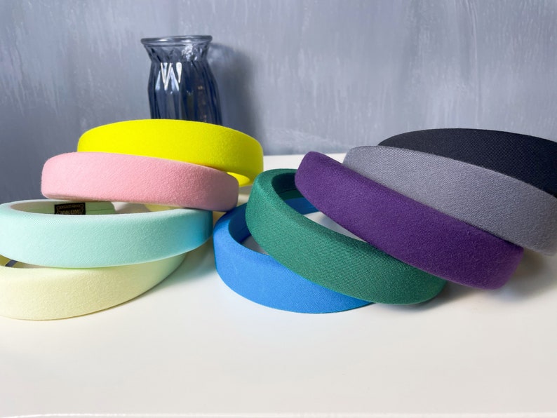 May include: A set of eight wide headbands in various colors, including yellow, pink, light blue, light green, blue, green, purple, and gray. The headbands are made of a soft, plush material.