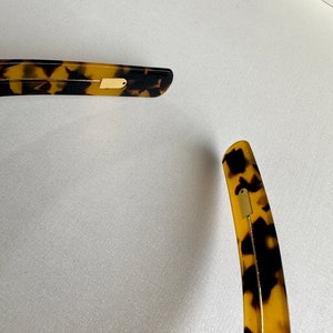 May include: A pair of tortoiseshell hair clips with gold accents. The clips are curved and have a smooth finish.