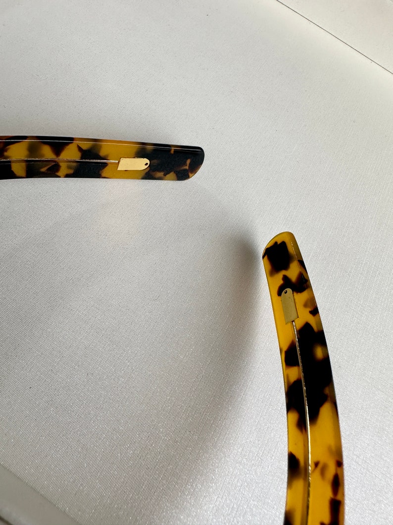 May include: A pair of tortoiseshell hair clips with gold accents. The clips are curved and have a smooth finish.
