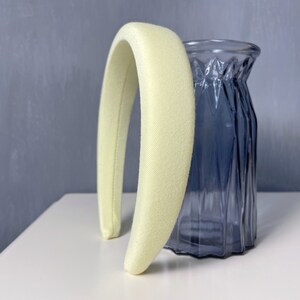 May include: A pale yellow padded headband for hair. The headband is made of a soft, smooth fabric and is curved to fit the head.