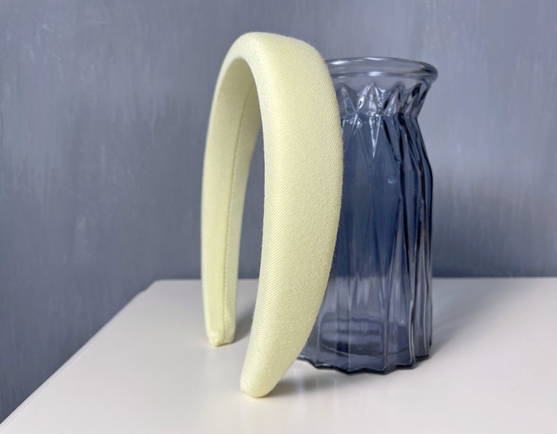 May include: A pale yellow padded headband for hair. The headband is made of a soft, smooth fabric and is curved to fit the head.