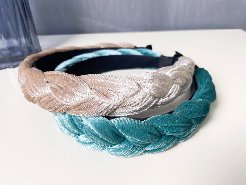May include: Two braided velvet headbands, one in a light beige color and the other in a teal blue color.