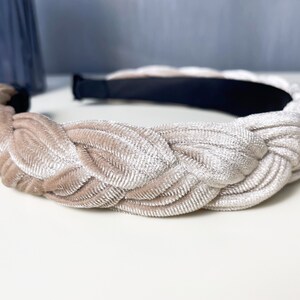 May include: A braided headband made of a soft, light beige velvet fabric. The headband is designed to be worn around the head and has a simple, elegant style.
