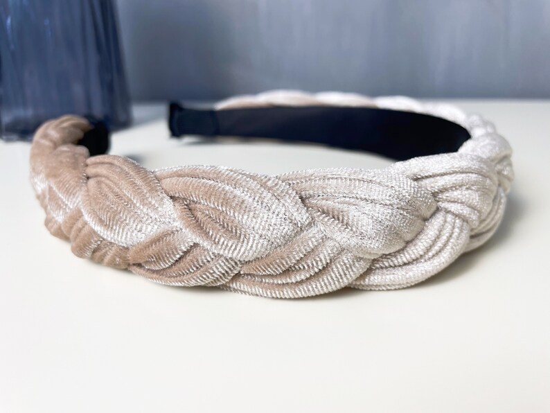 May include: A braided headband made of a soft, light beige velvet fabric. The headband is designed to be worn around the head and has a simple, elegant style.