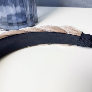 May include: A beige velvet headband with a black elastic band. The headband is braided and has a soft, luxurious feel.
