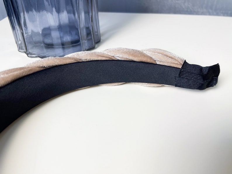 May include: A beige velvet headband with a black elastic band. The headband is braided and has a soft, luxurious feel.