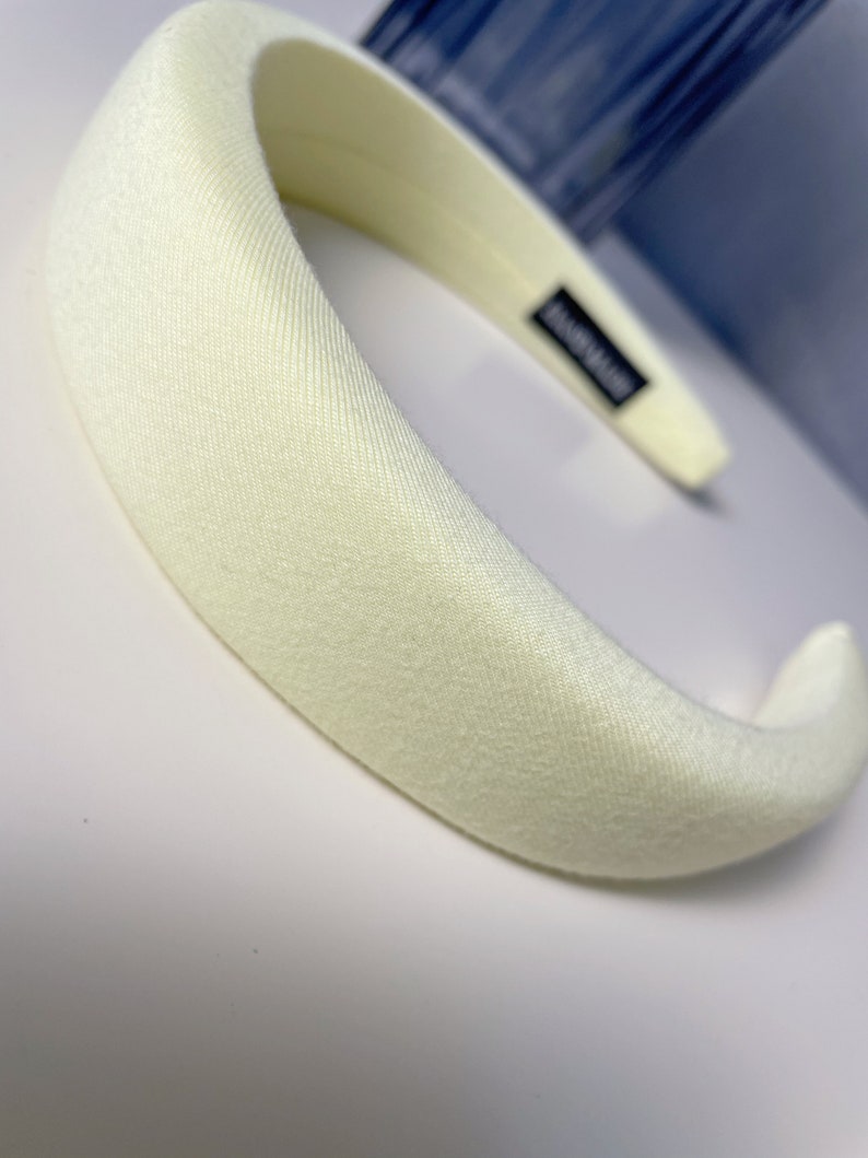May include: A wide, off-white headband made of a soft, textured fabric. The headband is curved and has a smooth, polished finish.