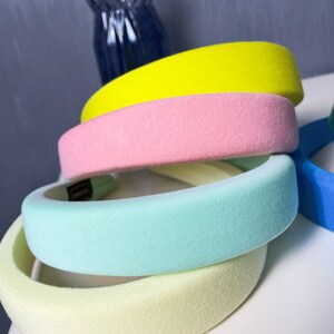 May include: Four velvet headbands in different pastel colors: yellow, pink, light blue, and light yellow. The headbands are stacked on top of each other.