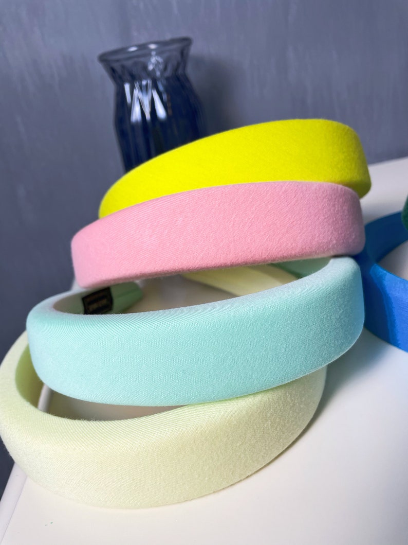 May include: Four velvet headbands in different pastel colors: yellow, pink, light blue, and light yellow. The headbands are stacked on top of each other.
