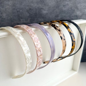 May include: A set of six plastic headbands in various colors and patterns, including white, pink, purple, brown, and leopard print. The headbands are displayed on a white surface.
