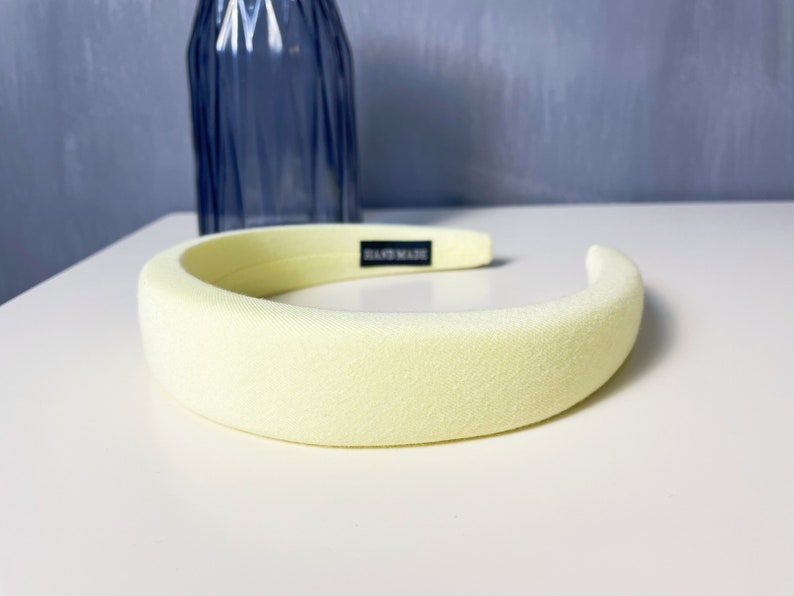 May include: A pale yellow headband with a black "Handmade" label. The headband is made of a soft, padded material.